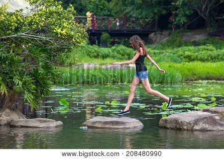 Girl jumping on stones in the lake. Jumping woman in the Yanoda National Park, Hainan, China.