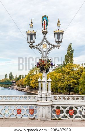 Old twin Lamp Lights on a single lamp post on the Bridge with white railings and small red shields over the River Ouse in York North Yorkshire England UK.