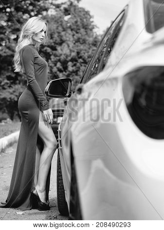 Young woman attractive sensual model with blonde hair and long gorgeous legs dressed in sexy green dress posing near white car outdoor