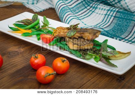 Fried fish with pea pods and cherry tomatoes. Wooden background. Close-up. Top view