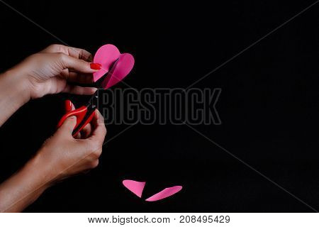 The picture is made on a dark background. The woman cuts the paper heart.
