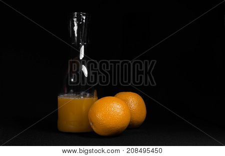 Transparent bottle with fresh orange juice. Two whole oranges nearby.