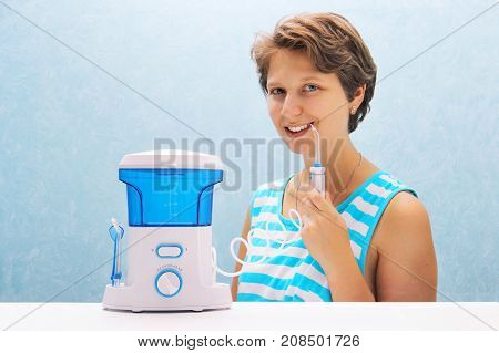 Beautiful Girl Flushes Her Teeth With An Oral Irrigator. The Woman Smiles And Holds The Irrigator Ha