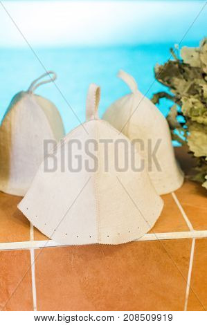 Three Russian White Wool Hats for Sauna Banya Bath House on a blue pool background. Bath accessories in traditional Russian sauna. concept of men's rest.
