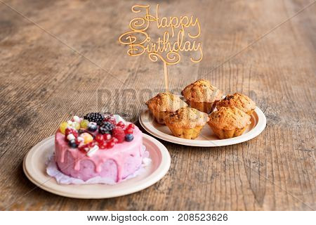 Birthday cake and muffins with wooden greeting sign on rustic background. Wooden sing with letters Happy Birthday and holiday sweets