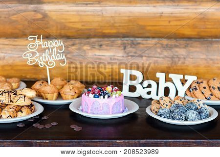 Birthday cakes and muffins with wooden greeting signs on rustic background. Wooden sing with letters Happy Birthday, Baby and holiday sweets