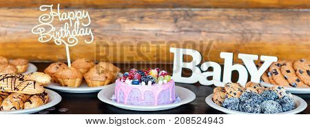 Birthday cakes and muffins with wooden greeting signs on rustic background. Wooden sing with letters Happy Birthday, Baby and holiday sweets