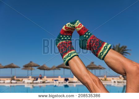 Christmas sock on palm tree at exotic tropical beach. Holiday concept for New Years Cards. Christmas sock on a sunlit legs of attractive women in background pool and palm trees