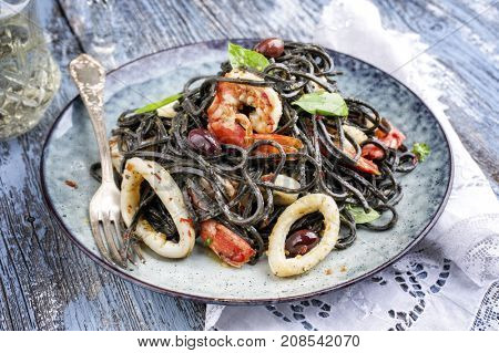 Italian linguine con tinta de calamari and prawns with olives as close-up on a plate 