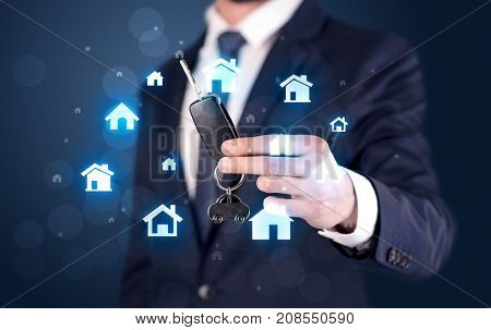 Businessman in suit holding keys with house graphics around and dark background