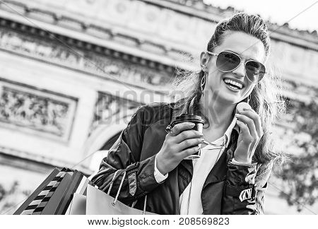 Stylish autumn in Paris. smiling trendy fashion-monger in sunglasses with shopping bags near Arc de Triomphe in Paris France having coffee and macaroon