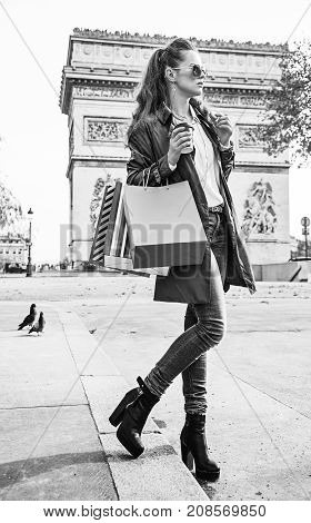 Stylish autumn in Paris. trendy woman in trench coat near Arc de Triomphe in Paris France with shopping bags having coffee and macaroon