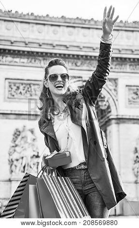 Stylish Christmas in Paris. happy trendy woman in trench coat with shopping bags and Christmas present in Paris France looking into the distance and handwaving