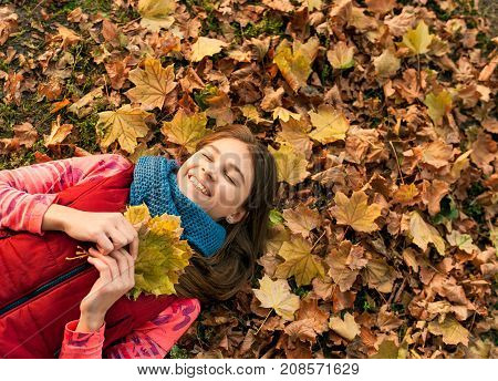 Pretty girl with long hair lying on the leaves in autumn. Girl lying in autumn with falling leaves wondering about something. Portrait of a beautiful smiling teenager. Autumn winter season.