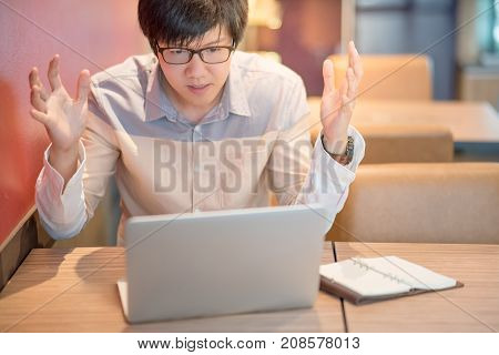 Young Asian business man feeling stressed angry and headache during working with laptop computer in cafe. freelance lifestyle in workspace.