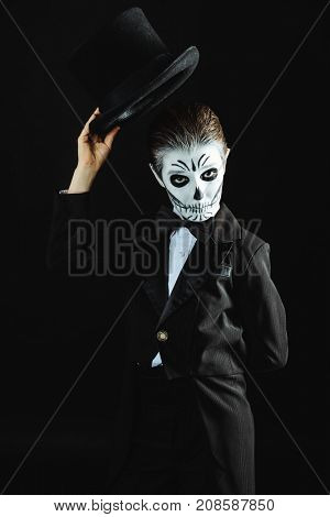 Portrait of a child boy with carnival make-up of a skeleton wearing elegant tail-coat. Studio shot over black background. Halloween. Dia de los muertos. The Day of the Dead.