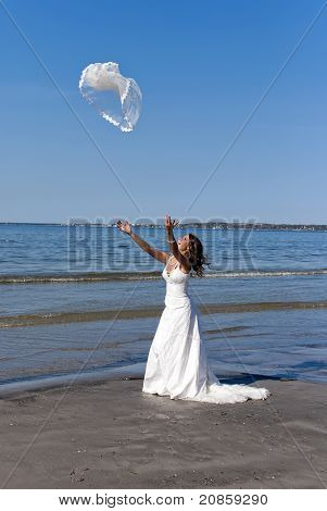 Belle jeune mariée jetant le voile près de la mer