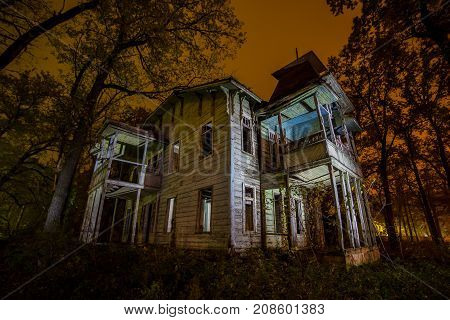 Old creepy wooden abandoned haunted mansion at night