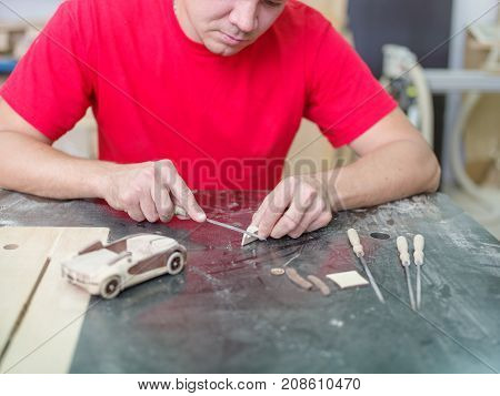 Master in red uniform with various tools collects a wooden car model