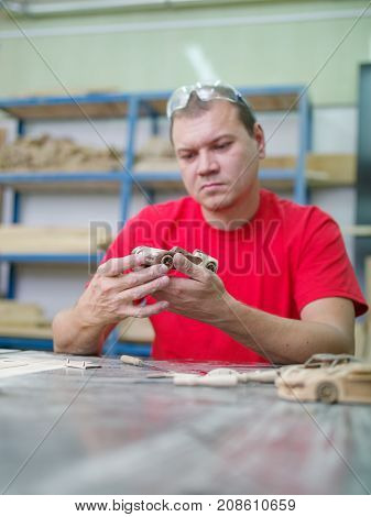 Master in a red uniform closeup of various tools collects a wooden model of a car