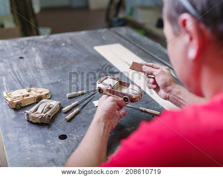 Master in a red uniform closeup of various tools collects a wooden model of a car