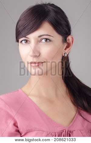 Closeup portrait of beautiful smiling young brunette Caucasian woman with brown eyes looking in camera. Girl female with long dark hair in pink dress. Studio beauty shot.
