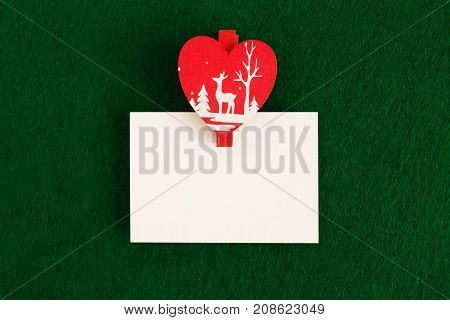 White sheet with red and white wooden pin on the green background for Christmas greetings. Copy space.