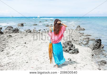 attractive boho styled young cheerful woman walking on the beach