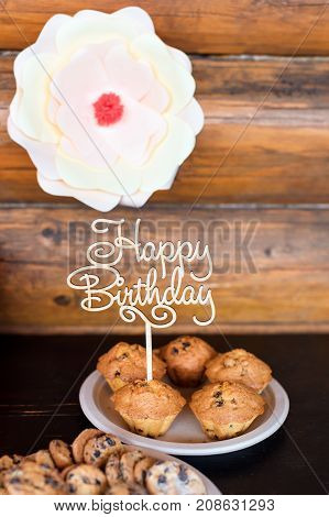 Birthday cakes and muffins with wooden greeting sign on rustic background. Wooden sing with letters Happy Birthday and holiday sweets