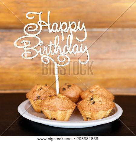 Birthday cakes and muffins with wooden greeting sign on rustic background. Wooden sing with letters Happy Birthday and holiday sweets