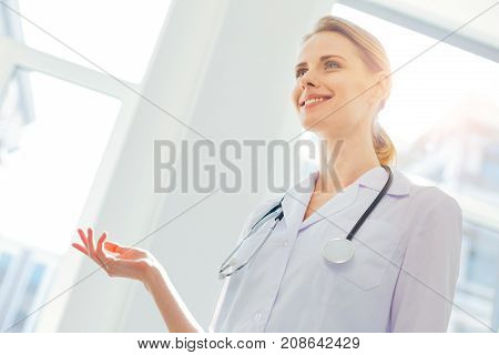 No time for worries. Low angle shot of a female practitioner wearing a white coat gesturing while looking into vacancy with a cheerful smile on her face.