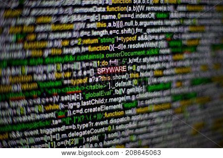 Macro photo of computer screen with program source code and highlighted SPYWARE inscription in the middle. Computer script on the screen with virus in it. Cyber security concept.