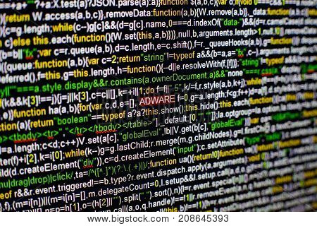 Macro photo of computer screen with program source code and highlighted ADWARE inscription in the middle. Computer script on the screen with virus in it. Cyber security concept.