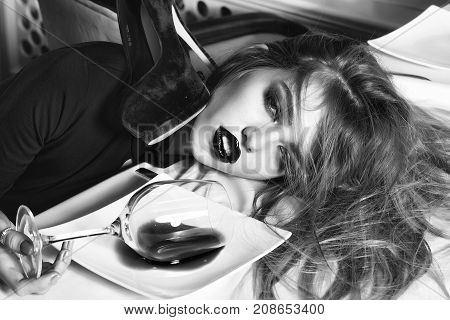 Sensual elegant glamour young drunk woman with beautiful hair lying on table with glass and poored red wine in plate after hangover with suide shoe horizontal picture