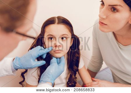 Want to sleep. Attentive mother raising her eyebrows and siting near her child while listening doctor