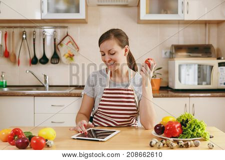 A Young Woman Siting By The Table And Looking For A Recipe In The Tablet In The Kitchen. Vegetable S