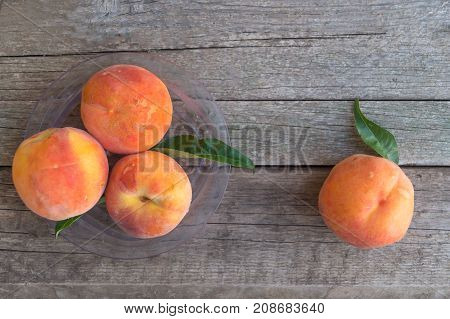 Ripe peaches with green leaves in a plastic plate on the old wooden background