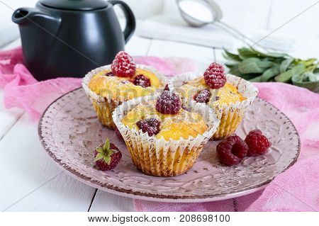 Delicious curd muffins with fresh raspberries decorated with powdered sugar on a ceramic plate.