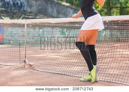 Beautiful legs of an athlete girl in a short skirt near a tennis net.