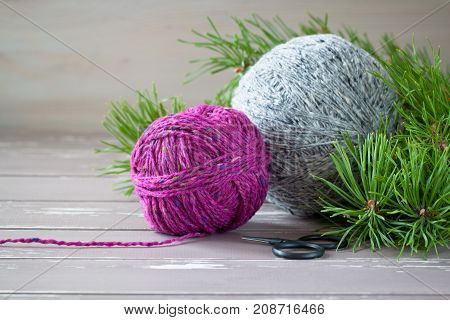 Fuchsia and grey tweed yarn on the wooden background near branches of pine-tree with black vintage scissors