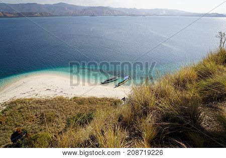 Top view of two boats at the coast of a white sand beach surrounded by blue turquoise colored ocean water in Flores Indonesia.