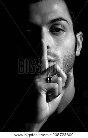 Hush sign. Young man showing silence sign with his index finger in front nose. Black and white.