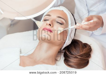 High-angle close-up view of the face of a beautiful woman during anti-aging facial massage with soft brushes in a modern cosmetic center