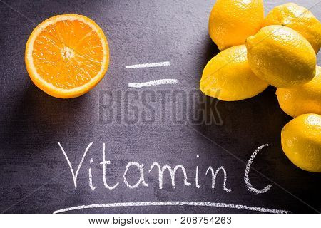 Orangei and group of lemons with equal sign and word vitamin C written by white chalk on black slate.