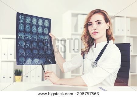 Attractive young doctor with red hair is showing an x ray while sitting in her office. Concept of a health care system Toned image