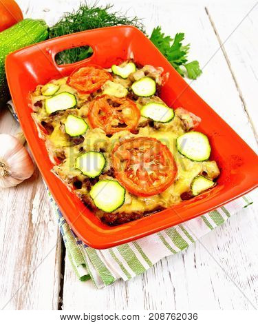 Casserole from minced meat, tomatoes and zucchini in a brazier on a napkin on a light wooden board background