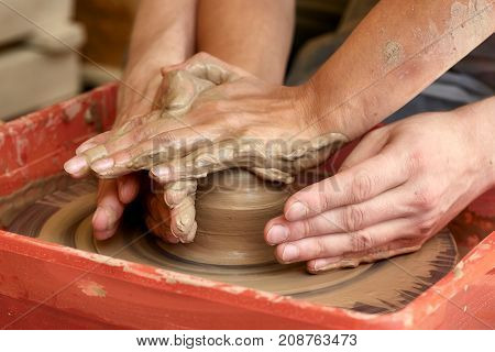 Hands of two people create pot on potter's wheel. Teaching pottery carftman's hands guiding