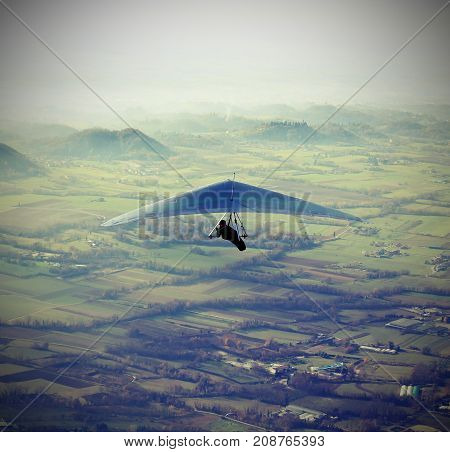 man flying high with his hang glider above the plain with vintage effect