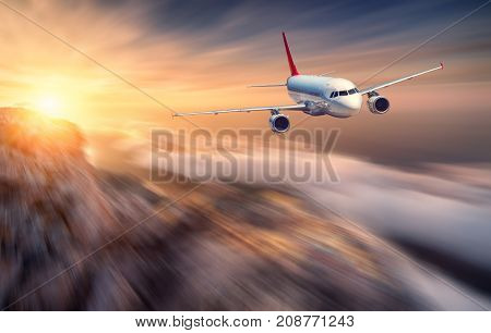 Airplane mith motion blur effect is flying over low clouds at sunset. Landscape with passenger airplane, blurred clouds, mountains, sun. Passenger aircraft. Business travel. Commercial plane. Concept