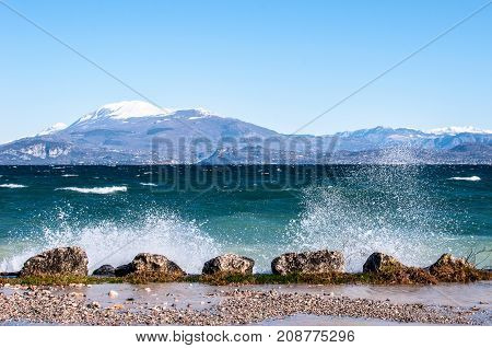 Landscape of a lake with waves and squirts on a windy day background with alpine mountains